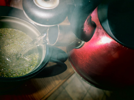 A view of steaming hot water being poured from tea kettle into a french press filled with loose leaf Yerba Mate.の写真素材