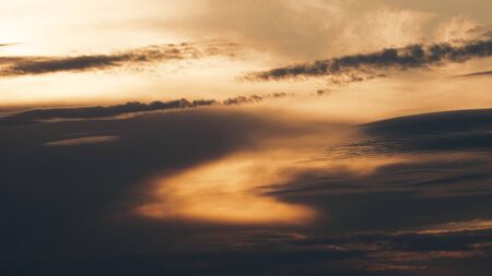 A warm toned view of the sun setting behind a cloudy sky.の写真素材