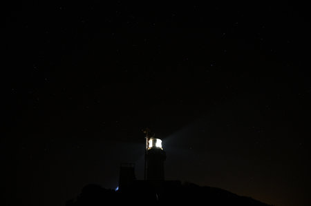 Lighthouse at night with starry sky and moon in the background
