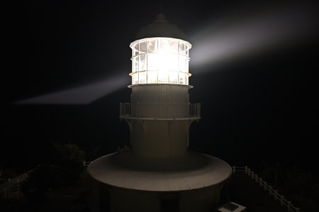Lighthouse at night with a light beam in the foreground and a dark backgroundの写真素材