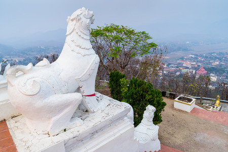 White Thai art lions at entrance of Wat Phra That Doi Gongmu with view of Maehongson city in evening periodの写真素材