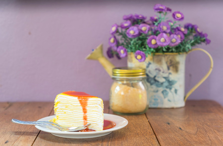 Strawberry crape cake on white dish with artificial flower and vase decoration on wooden table with...