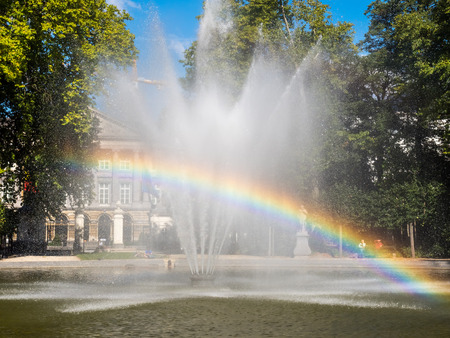 Artificial fountain with reflected bubble water rainbow in natural park under clear blue skyの写真素材
