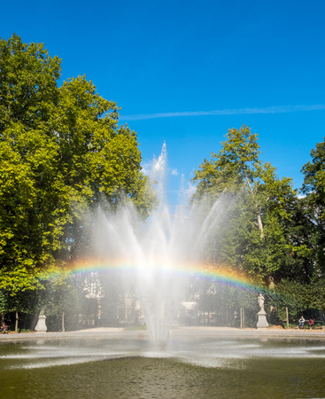 Artificial fountain with reflected bubble water rainbow in natural park under clear blue skyの写真素材