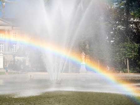 Artificial fountain with reflected bubble water rainbow in natural park under clear blue skyの写真素材