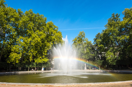 Artificial fountain with reflected bubble water rainbow in natural park under clear blue skyの写真素材