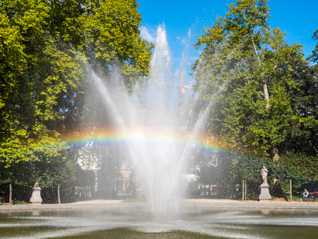 Artificial fountain with reflected bubble water rainbow in natural park under clear blue skyの写真素材