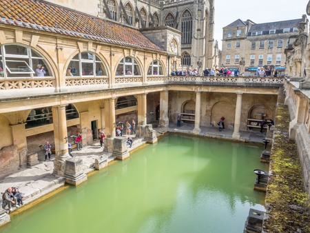 BATH - MAY 19 : Roman Bath, the UNESCO World Heritage site, with The Bath Abbey behind under cloudy sky and green colour water in Roman Bathのeditorial素材