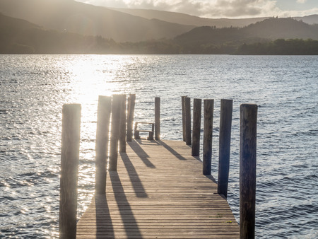 Timber bridge at lake coast under sunset evening cloudy skyの写真素材
