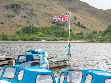 Yacht in rural pier in lake with mountain background under cloudy sky in countryside of Englandの写真素材