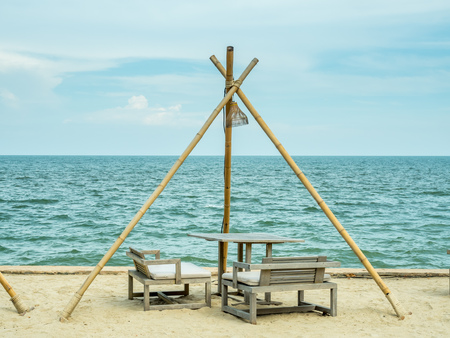 Wooden bench and table on sand beside the sea under cloudy evening skyの写真素材