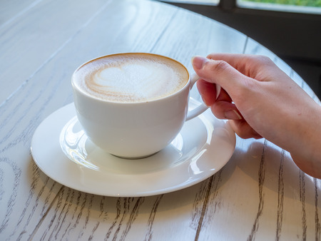 Coffee with milk, known as Latte or cafe au lait, in white cup drink with breakfast in morning time, and lady's hand touch on cup earの写真素材
