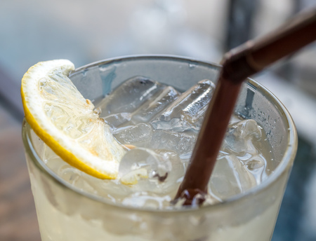 Fresh cold soda lemonade with ice and straw in glass on wooden table in cafeの写真素材