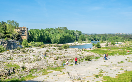 NIMES, FRANCE - APRIL 12 : Tourists at bank of Gardon river beneath Pont du Gard, ancient Roman aqueduct, under blue sky in Nimes, France, on April 12, 2017.のeditorial素材
