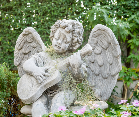Playing guitar little angel statue in outdoor garden under evening lightの写真素材