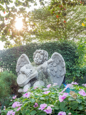 Playing guitar little angel statue in outdoor garden under evening lightの写真素材