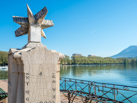 ANNECY, FRANCE - APRIL 14 : Outdoor sundial in park nearby lake with mountains view background in...
