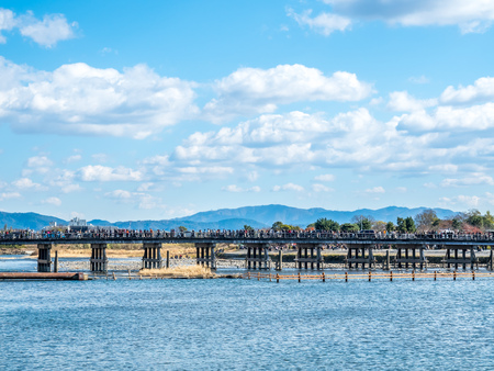 Famous bridge cross river in Arashiyama region in Kyoto, Japan, in autumn season under cloudy blue skyの写真素材