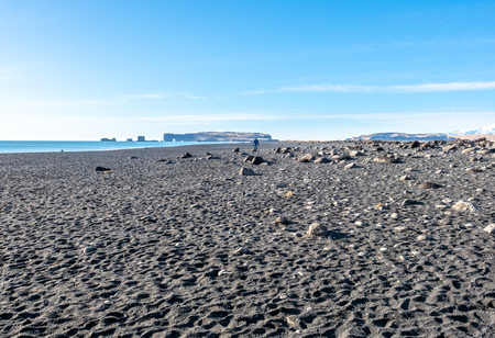 Reynisfjara black sand beach is landmark of Vik town in Iceland, fine black sand with small stones on beach with mountain and islands in background, under blue sky in winter seasonの写真素材
