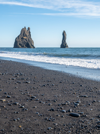 Reynisfjara black sand beach is landmark of Vik town in Iceland, fine black sand with small stones on beach with mountain and islands in background, under blue sky in winter seasonの写真素材