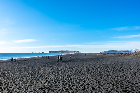 Reynisfjara black sand beach is landmark of Vik town in Iceland, fine black sand with small stones on beach with mountain and islands in background, under blue sky in winter seasonの写真素材