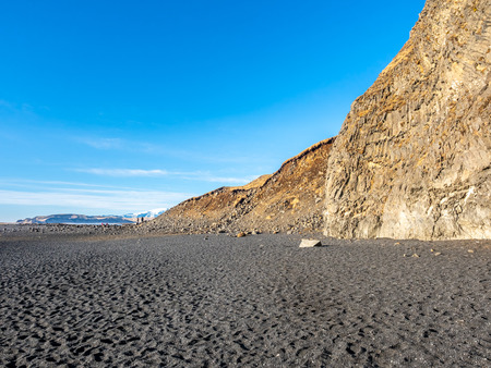Reynisfjara black sand beach is landmark of Vik town in Iceland, fine black sand with small stones on beach with mountain and islands in background, under blue sky in winter seasonの写真素材