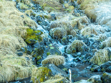 Small flow of water in river near Seljalandsfoss waterfall with snow and ice on rock in winter season in Icelandの写真素材