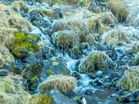 Small flow of water in river near Seljalandsfoss waterfall with snow and ice on rock in winter season in Icelandの写真素材