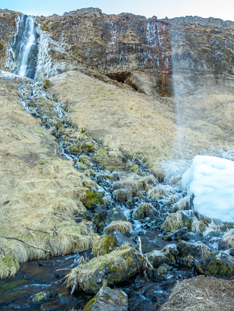 Large waterfall near Seljalandsfoss waterfall with large snow with small ascending fountain, in winter season in Icelandの写真素材