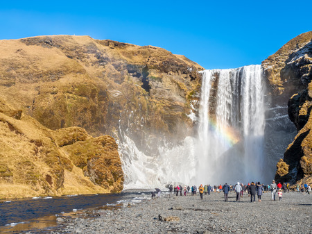 ICELAND - MARCH 3 : Skogafoss waterfall with rainbow refraction, with snow and ice in winter season and crowded with tourists in Iceland, on March 3, 2018.のeditorial素材