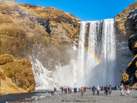 ICELAND - MARCH 3 : Skogafoss waterfall with rainbow refraction, with snow and ice in winter season and crowded with tourists in Iceland, on March 3, 2018.のeditorial素材