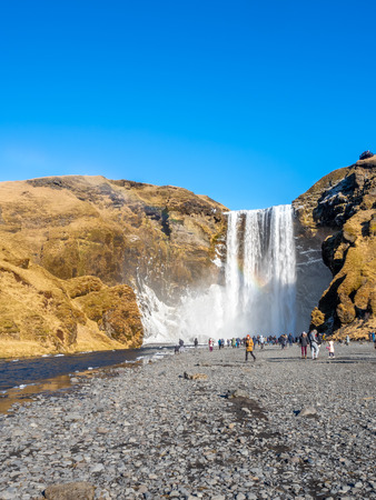 ICELAND - MARCH 3 : Skogafoss waterfall with rainbow refraction, with snow and ice in winter season and crowded with tourists in Iceland, on March 3, 2018.のeditorial素材
