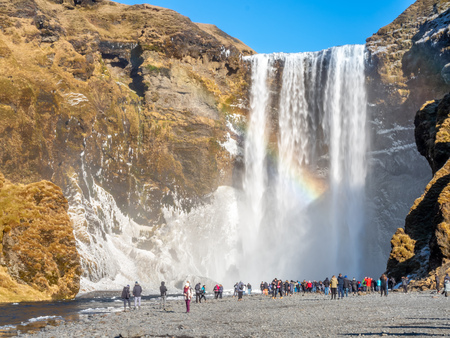 ICELAND - MARCH 3 : Skogafoss waterfall with rainbow refraction, with snow and ice in winter season and crowded with tourists in Iceland, on March 3, 2018.のeditorial素材