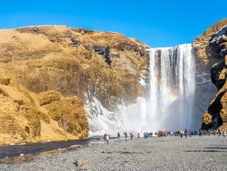 ICELAND - MARCH 3 : Skogafoss waterfall with rainbow refraction, with snow and ice in winter season and crowded with tourists in Iceland, on March 3, 2018.のeditorial素材