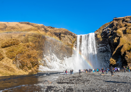 ICELAND - MARCH 3 : Skogafoss waterfall with rainbow refraction, with snow and ice in winter season and crowded with tourists in Iceland, on March 3, 2018.のeditorial素材