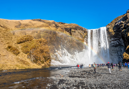 ICELAND - MARCH 3 : Skogafoss waterfall with rainbow refraction, with snow and ice in winter season and crowded with tourists in Iceland, on March 3, 2018.のeditorial素材