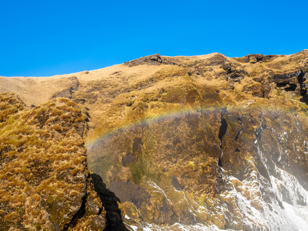 Skogafoss, large waterfall landmark in Iceland, with rainbow refraction, in winter season, with snow and iceの写真素材