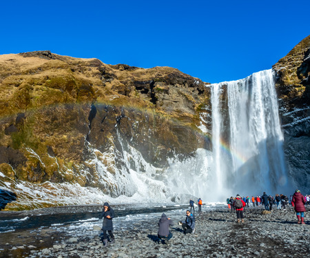 ICELAND - MARCH 3 : Skogafoss waterfall with rainbow refraction, with snow and ice in winter season and crowded with tourists in Iceland, on March 3, 2018.のeditorial素材