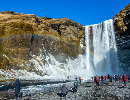 ICELAND - MARCH 3 : Skogafoss waterfall with rainbow refraction, with snow and ice in winter season and crowded with tourists in Iceland, on March 3, 2018.のeditorial素材