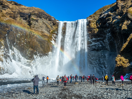 ICELAND - MARCH 3 : Skogafoss waterfall with rainbow refraction, with snow and ice in winter season and crowded with tourists in Iceland, on March 3, 2018.のeditorial素材