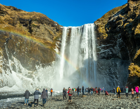 ICELAND - MARCH 3 : Skogafoss waterfall with rainbow refraction, with snow and ice in winter season and crowded with tourists in Iceland, on March 3, 2018.のeditorial素材