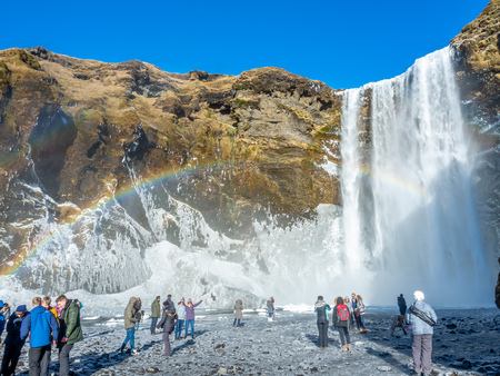ICELAND - MARCH 3 : Skogafoss waterfall with rainbow refraction, with snow and ice in winter season and crowded with tourists in Iceland, on March 3, 2018.のeditorial素材