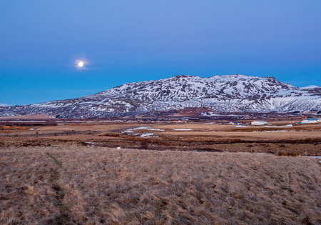 Mountain, field in twilight evening sky with full moon night light in winter season in Icelandの写真素材