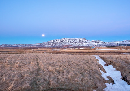 Mountain, field in twilight evening sky with full moon night light in winter season in Icelandの写真素材