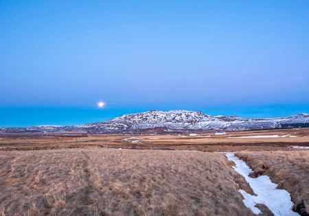 Mountain, field in twilight evening sky with full moon night light in winter season in Icelandの写真素材