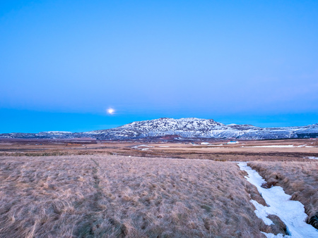 Mountain, field in twilight evening sky with full moon night light in winter season in Icelandの写真素材