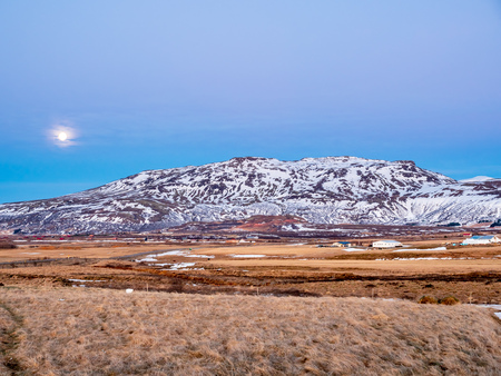 Mountain, field in twilight evening sky with full moon night light in winter season in Icelandの写真素材