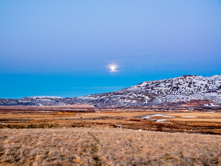 Mountain, field in twilight evening sky with full moon night light in winter season in Icelandの写真素材