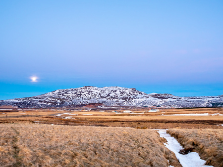 Mountain, field in twilight evening sky with full moon night light in winter season in Icelandの写真素材