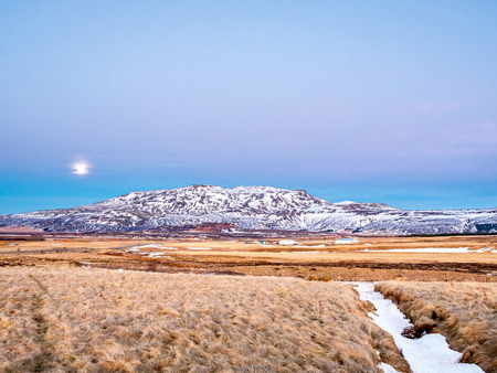 Mountain, field in twilight evening sky with full moon night light in winter season in Icelandの写真素材